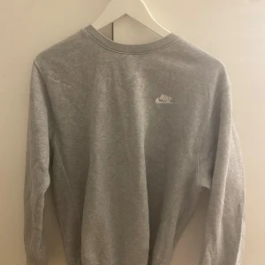 Grå sweatshirt från Nike - Klassisk grå sweatshirt från Nike med rund halsringning och diskret Nike-logga på bröstet. Perfekt för en avslappnad stil och enkel att matcha med det mesta. Mjuk och bekväm bomullskänsla passar både s och m.