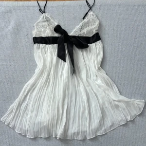 Victoria secret babydoll spetstopp  - Säljer en vit plisserad linnetopp från Victoria's Secret med spets upptill och en svart rosett under bysten. Tunna axelband och romantisk känsla. Perfekt för dig som gillar feminina detaljer. Köpt för ca 800 kr och aldrig använd💞