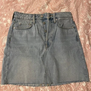Ljusblå jeanskjol med knappar - Säljer en ljusblå jeanskjol med rå kant nertill och knappar framtill. Kjolen har klassiska jeansfickor både fram och bak samt bälteshällor. Perfekt att styla med en enkel topp eller hoodie.