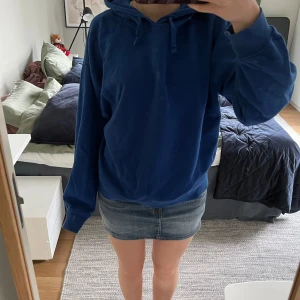 Blå hoodie med huva och snörning - Mysig blå hoodie med huva och snörning i halsen. Tröjan har en loose passform och långa ärmar, perfekt för chill dagar. Enkel och stilren design som funkar till det mesta. Snygg att matcha med jeans eller kjol.