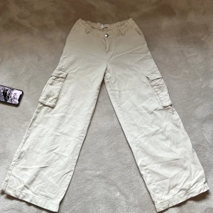 Beiga cargopants från Lindex - Säljer ett par beiga cargopants från Lindex med bred passform och stora fickor på sidorna. Byxorna har knapp och dragkedja framtill samt hällor för bälte. Perfekta för en avslappnad och trendig stil. Knappt andvända, säljer då dom blivit försmå! Hör av er om ni har frågor eller för intresse❤️
