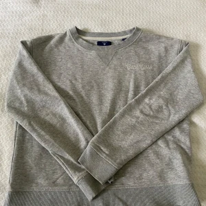 Ljusgrå sweatshirt från Gant - Säljer en stilren ljusgrå sweatshirt från Gant med broderad logga på bröstet. Skulle säga att den passar storlek XS, men den är i 15 år/170cm!🥰
