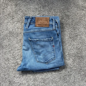 Replay Anbass jeans i ljusblå denim - Säljer ett par Replay Anbass jeans i ljusblå tvätt. Klassisk femficksmodell med normal passform och raka ben. Jeansbyxorna har läderpatch med Replay-logga bak och silverfärgad knapp framtill. Kontakta oss på Valmont för mer frågor eller prisförslag🙌
