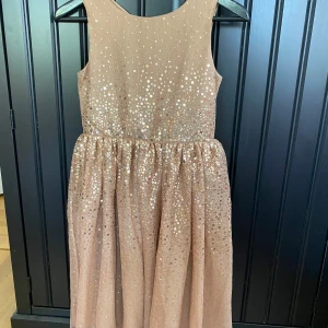 Champagnefärgad glittrig klänning från H&M stl 140 barn  - Superfin champagnefärgad klänning från H&M med glittriga paljetter över hela ovandelen och kjolen. Ärmlös modell med rund halsringning och lätt utställd kjol. Perfekt för speciella tillfällen när du vill glänsa extra.