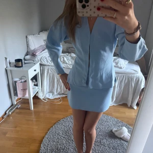 Ljusblå kostym med kjol - Säljer en ljusblå kostym med kavaj och matchande kjol. Kavajen har en stilren design utan synliga knappar och en v-ringad öppning framtill. Kjolen är rak och slutar ovanför knäna. Säljs för 500kr tsm, annars 300kr för toppen och 300kr för kjolen🩵endast använt ett fåtal gånger