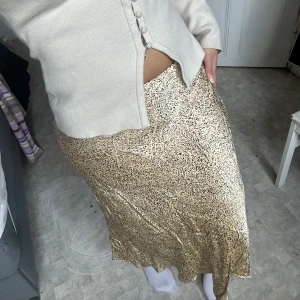 Gul leopardmönstrad satinkjol  - Säljer en glansig gul satinkjol med leopardmönster. Kjolen har en lång, rak passform och sitter snyggt i midjan. Perfekt för dig som vill sticka ut med ett coolt mönster och mjukt material.