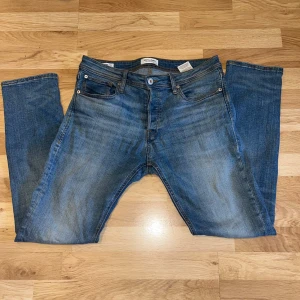 Blå jeans från Jack & Jones - Klassiska blå jeans från Jack & Jones med fem fickor och raka ben. Jeansen har en snygg tvätt med lätt slitning framtill och bak, samt orangea sömmar. Passar perfekt till vardagsstilen och har en normal passform.