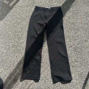 Svarta kostymbyxor med raka ben - Snygga svarta kostymbyxor med klassisk passform.Byxorna har normal midja och stängs med dragkedja och knapp framtill. Perfekta till en stilren look.