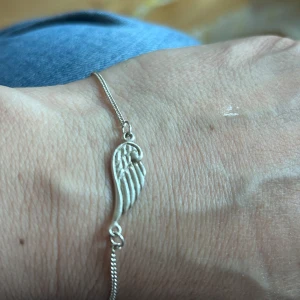 Silver  armband med änglavinge - Säljer ett stilrent armband i silverr 925 med en detalj i form av en änglavinge. Perfekt som en fin accessoar till din outfit. Kedjan är tunn och smidig, och vingen har fina detaljer.
