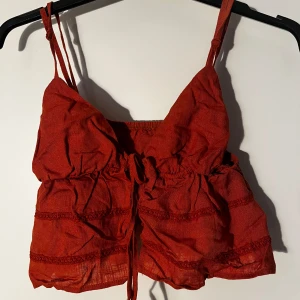 Röd croppad linnetopp med knyt - Säljer en röd croppad linnetopp med smala axelband och knyt framtill. Toppen har volangdetaljer perfekt för sommaren. Snygg och luftig modell som passar till många olika outfits.