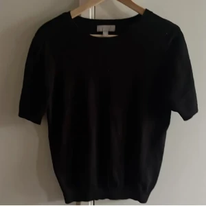 Svart kortärmad stickad tröja - En enkel och stilren svart stickad tröja med korta ärmar och rund hals. Perfekt att matcha med jeans eller kjol för en clean look. Ribbstickade muddar vid ärmslut och nederkant💕