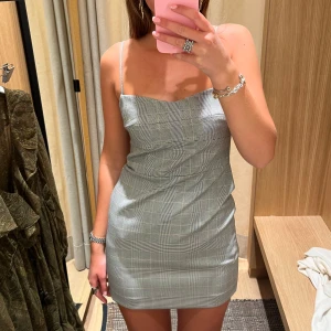 Grå kortklänning med tunna axelband - Säljer en helt oanvänd, snygg grå kortklänning med tunna axelband och rutigt mönster💓