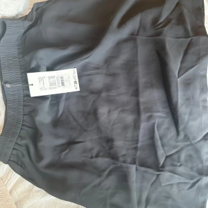 Svart kjol från Kaffe - Enkel svart kjol från kaffe med resår i midjan. parachute-material. Kjolen har en rak passform och är tillverkad i ett mjukt, lätt tyg som ger en avslappnad känsla. Perfekt att styla med en t-shirt eller hoodie.