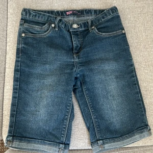 Levi's Bermuda jeansshorts - Mörkblå jeansshorts från Levi's i bermudamodell med klassiska fem fickor och snygga detaljer på bakfickorna. Shorts med normal passform och knappgylf, perfekta för sommaren.