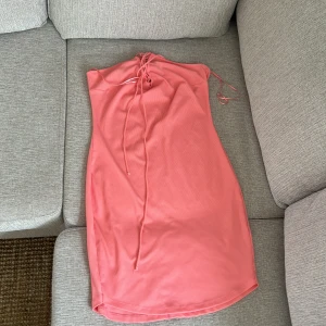 Rosa ribbad klänning från Gina Tricot - Säljer en rosa ribbad klänning från Gina Tricot i storlek M. Klänningen har smala axelband och snörning framtill vid halsen för en snygg detalj. Perfekt för varma dagar och enkel att styla med sneakers eller sandaler.