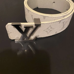 Louis Vuitton vitt bälte med silverfärgat LV-spänne - Säljer ett vitt Louis Vuitton-bälte med klassiskt silverfärgat LV-spänne. Bältet har diskret monogrammönster och är tillverkat i präglat skinn. Perfekt accessoar för att lyfta din outfit.