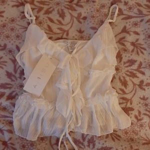 Vit volangprydd linnetopp från Aisu - Supersöt vit linnetopp från Aisu med volangdetaljer och knyt framtill. Perfekt för varma dagar och somriga outfits.  Har 2 lager med tyg så den syns inte igenom.🥂🩷