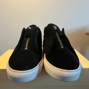 Arigato skor clean zip 90 st 45 - Säljer ett par svarta sneakers från Axel Arigato i mocka med vit platt sula och dragkedja framtill istället för klassisk snörning.  Passar flera storlekar 