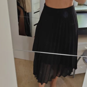 Svart plisserad kjol från Stradivarius - Säljer en svart plisserad kjol från Stradivarius i storlek 36. Kjolen är lång, har asymmetrisk nederkant och är tillverkad i ett lätt, transparent material med underkjol. Perfekt för dig som gillar flowiga och stilrena plagg.