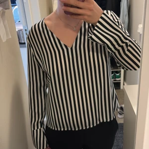 Svartvit randig blus med öppen rygg - En svartvit randig blus från Gina. Den har en v rigning fram och öppen rygg. Perfekt till tillfällen när man vill klä upp sig men ändå hålla det diskret.