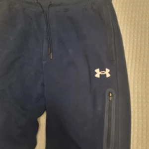 Mörkblå byxor från Under Armour - Säljer ett par mörkblå mjukisbyxor från Under Armour med dragsko i midjan och dragkedjeficka på sidan.