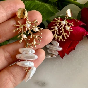 Guldiga örhängen med pärlor och korallinspirerad design - Unika örhängen i guldton med korallinspirerad form och vita pärlor. Hängande oregelbundna sötvattenspärlor ger ett coolt och trendigt uttryck. Perfekta för att sticka ut och ge en lyxig känsla till din look.