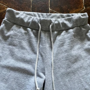 Ljusgrå mjukisbyxor - Säljer ett par ljusgrå mjukisbyxor med bred resår i midjan och snörning framtill. Byxorna har raka ben/ går ut lite och är tillverkade i mjukt material som passar perfekt för en avslappnad stil.