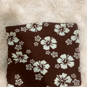 Brun blommig top - Säljer en brun top med stora vita blommor i ett tropiskt mönster. Kan också användas som kjol. Köpt i Spanien. 