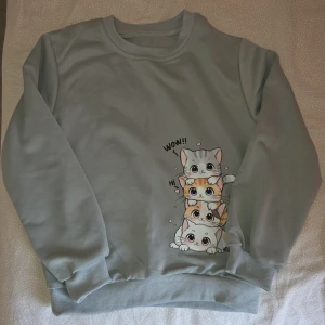Ljusgrå sweatshirt med kattmotiv - Supergullig ljusgrå sweatshirt med tryck av fyra tecknade katter staplade på varandra och texten 'WOW!!' och 'HI'. Tröjan har rund halsringning, långa ärmar och ribbade muddar vid ärmslut och nederkant.