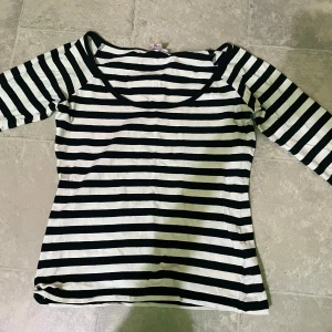 Svartvit randig topp - Säljer en svartvit randig topp med trekvartsärm och rund halsringning. Perfekt för en stilren och klassisk look. Tunn och mjuk i materialet, passar bra till jeans eller kjol.