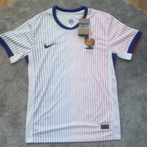 Frankrike fotbollströja - Säljer en matchtröja och shorts från Frankrikes landslag. Tröjan är vit med tunna blå och röda ränder, blå Nike-logga och FFF-märke med tupp. Shortsen är blå med vita och röda ränder samt FFF-logga. Båda i lätt och ventilerande material.
