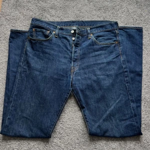 Levi's 501 jeans mörkblå W36 L36 - Klassiska Levi's 501 jeans i mörkblå denim med raka ben och knappgylf. Snygga kontrastsömmar, fem fickor och ikonisk läderpatch bak i midjan. Perfekta för dig som gillar tidlös stil och vill ha ett par jeans som funkar till allt.