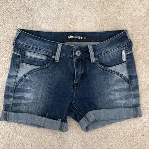 Mörkblå jeansshorts från Lab Industries - Snygga mörkblå jeansshorts från Lab Industries och uppvikta benslut. Klassisk femficksmodell med broderade bakfickor och tydliga sömmar. Perfekta för sommardagar och enkel att matcha med allt.