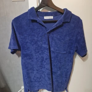 Blå frottéskjorta från Zara - Mjuk blå skjorta från Zara i frotté med klassisk krage och bröstficka. Perfekt för dig som gillar chill och avslappnad stil. Kortärmad modell som ger en cool vibe och passar till många outfits.