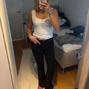 Svarta bootcut jeans - Säljer ett par svarta jeans med bootcut-modell och klassisk femficksdesign. Jeansen har låg midja och raka ben som blir lite utsvängda nertill. Perfekta för dig som gillar en tidlös och clean look. Materialet är jeans i bomull.