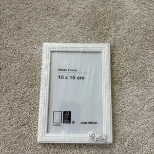 Foto ram - Det här är en fotoram från Clas Ohlson, storlek 10 x 15 cm. Perfekt för att visa upp dina favoritbilder på skrivbordet eller väggen. Enkel och stilren design som passar in i alla rum. Ramen är ny och fortfarande inplastad.