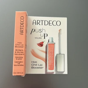 ARTDECO Hot Chili Lip Booster - Volymgivande läppglans med chili-effekt som ger push-up känsla och extra fylliga läppar. Kommer i en snygg genomskinlig tub med applikator och har en varm, persikotonad färg. Perfekt för dig som vill ha glansiga och plumpade läppar med lite sting.