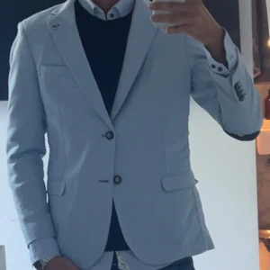 Ljusblå kavaj med mönstrat foder - Snygg ljusblå kavaj med två knappar framtill och coolt mönstrat innerfoder i blått, brunt och vitt. Kavajen har mörkblåa armbågslappar och klassiska fickor. Perfekt för dig som vill sticka ut med stilren look och unika detaljer. Bara att skriva om du har några frågor!