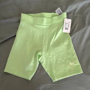 Ljusgröna tighta shorts från Nike - Nike biker shorts i ljusgrönt med hög midja och tight passform. Snyggt minimalistiskt Nike-logo tryckt på benet. Mjukt och stretchigt material som passar perfekt för träning eller chill. Midilängd och bred linning för extra komfort.
