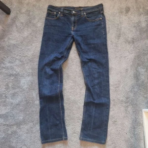 Blå jeans från Nudie Jeans Co - Snygga blå jeans från Nudie Jeans Co med klassisk femficksdesign och kontrastsömmar. Jeansen har rak passform och är tillverkade i bomull. Perfekta för dig som gillar stilrena och tidlösa jeans med en clean look.