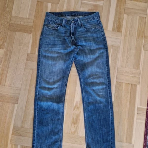 Levi's 505 blå jeans  - Klassiska Levi's 505 jeans i blå tvätt med snyggt slitna detaljer. Modellen har rak passform, fem fickor och normal midja. Jeansen är tillverkade i denim och har den ikoniska läderpatchen med en "vintage look" bak i midjan. Storlek 30 32