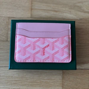Goy4rd plånbok - Supersnygg rosa plånbok med deras ikoniska grafiska mönster i ljusrosa och vitt. Plånboken har flera kortfack och är tillverkad i skinn och canvas. Perfekt för dig som vill ha något unikt och trendigt i väskan.
