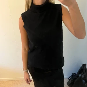 Svart ärmlös polotopp - Snygg svart polotopp utan ärmar med hög krage och rak passform. Toppen är stickad och har en clean, minimalistisk look som passar perfekt till både kjol och jeans. 