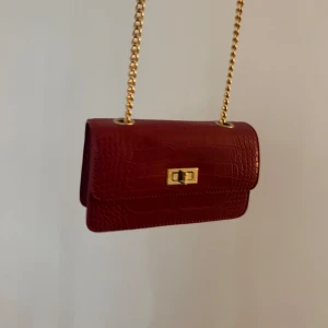 Röd axelväska med kedja - Snygg röd axelväska i skinnimitation med krokodilpräglad yta och guldfärgad kedja❣️