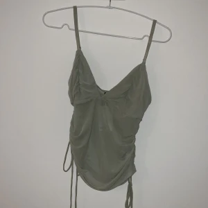 Grön mesh linnetopp från Divided - Snygg ljusgrön mesh linnetopp från Divided med smala axelband och trendig snörning i sidorna. Toppen har en draperad look framtill och är croppad, perfekt för att skapa en cool och avslappnad stil. Köpt på HM, plagget är oanvänt.