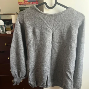 Grå stickad tröja med rund hals - Mysig grå stickad tröja med rundad hals och tre kvarts ärmar. Tröjan har ribbade muddar vid ärmslut och nederkant, vilket ger en chill och avslappnad vibe. Perfekt att slänga på sig när det är lite kyligt ute.