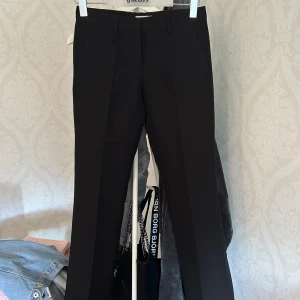 Svarta kostymbyxor från Nelly - Snygga svarta kostymbyxor från Nelly i klassisk rak modell. Byxorna har pressveck framtill, hällor för bälte och sidfickor. Perfekta för en clean och stilren look. Materialet känns mjukt och följsamt.