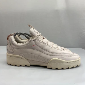 Beige sneakers från Reebok med chunky sula - Säljer ett par beige sneakers från Reebok med riktigt chunky och räfflad sula. Skorna har snygga sömdetaljer, diskreta röda inslag och snörning framtill. Ovandelen är i skinn och har en modern, sportig vibe som sticker ut.