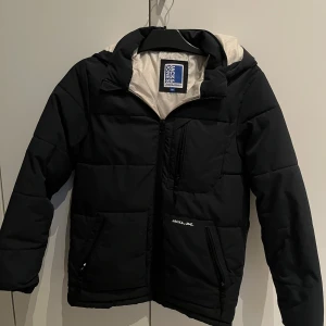 Svart pufferjacka från Jack & Jones - Svart pufferjacka från Jack & Jones med vit insida och huva. Jackan är perfekt nu inför hösten! Och har används endast en säsong. Men däremot så har jack & jones texten lossnat lite. Nypris ifrån jack and jones : 790 kr. Men jag säljer för 420 kr! Pris kan självklart diskuteras.