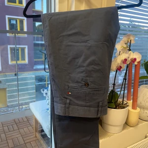 Chinos från Tommy Hilfiger - Blå chinos från Tommy Hilfiger i storlek 32/34. Byxorna har klassisk passform. 